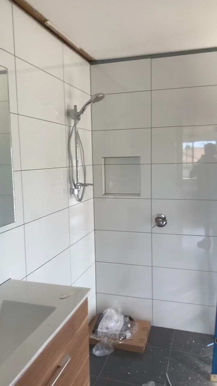 A white tiled shower with a rail shower and a built in niche