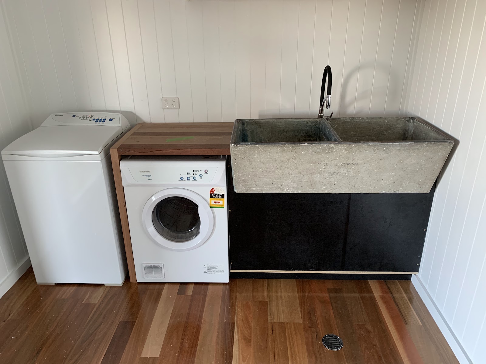 A laundry with a concrete look double tub, black gooseneck mixer and a washer and dryer