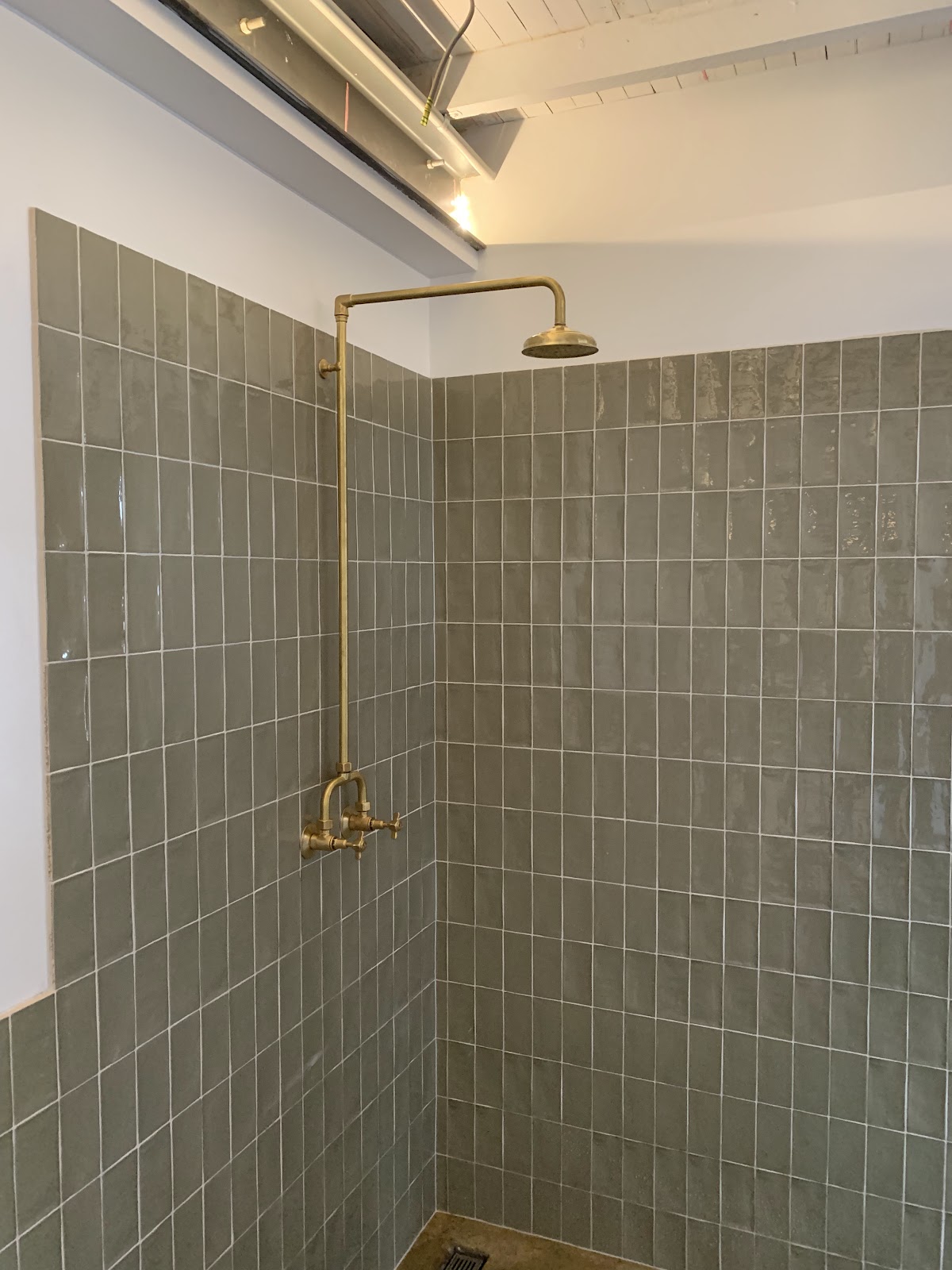 An exposed brass rain shower on sage green tiles, fitted by Jordin Watson Plumbing