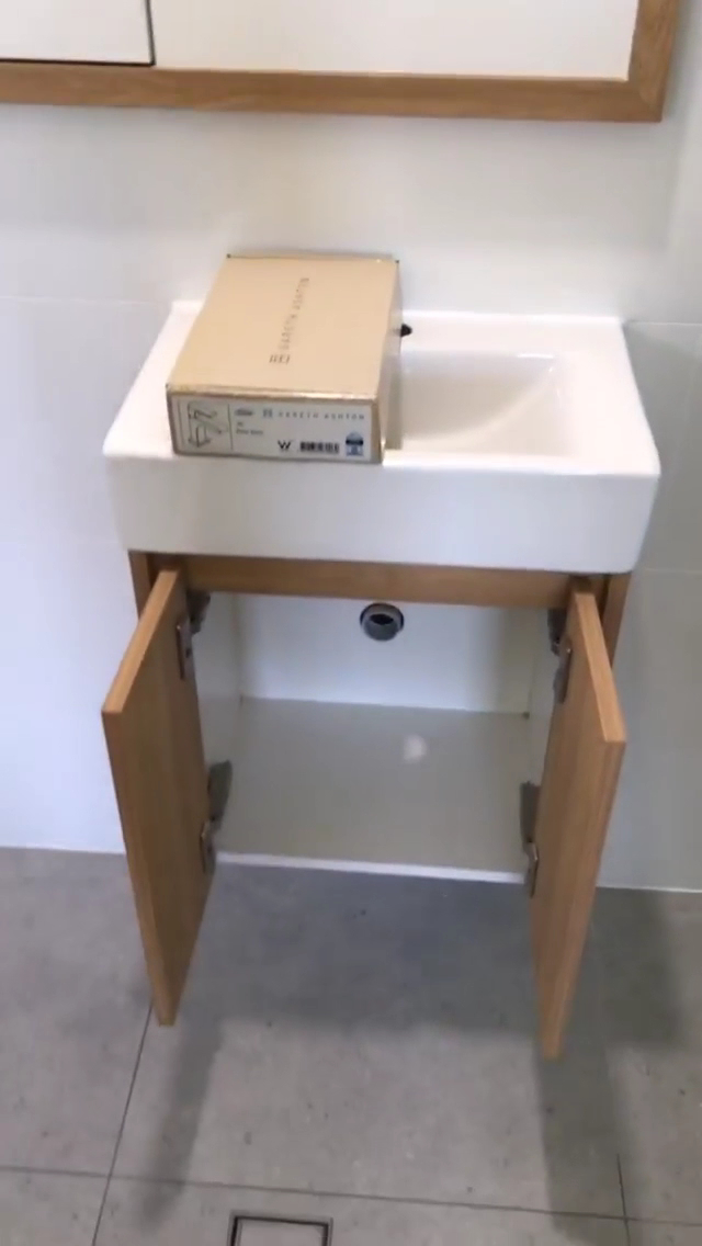 A new wall hung timber vanity with a white basin being fitted in a tiled bathroom